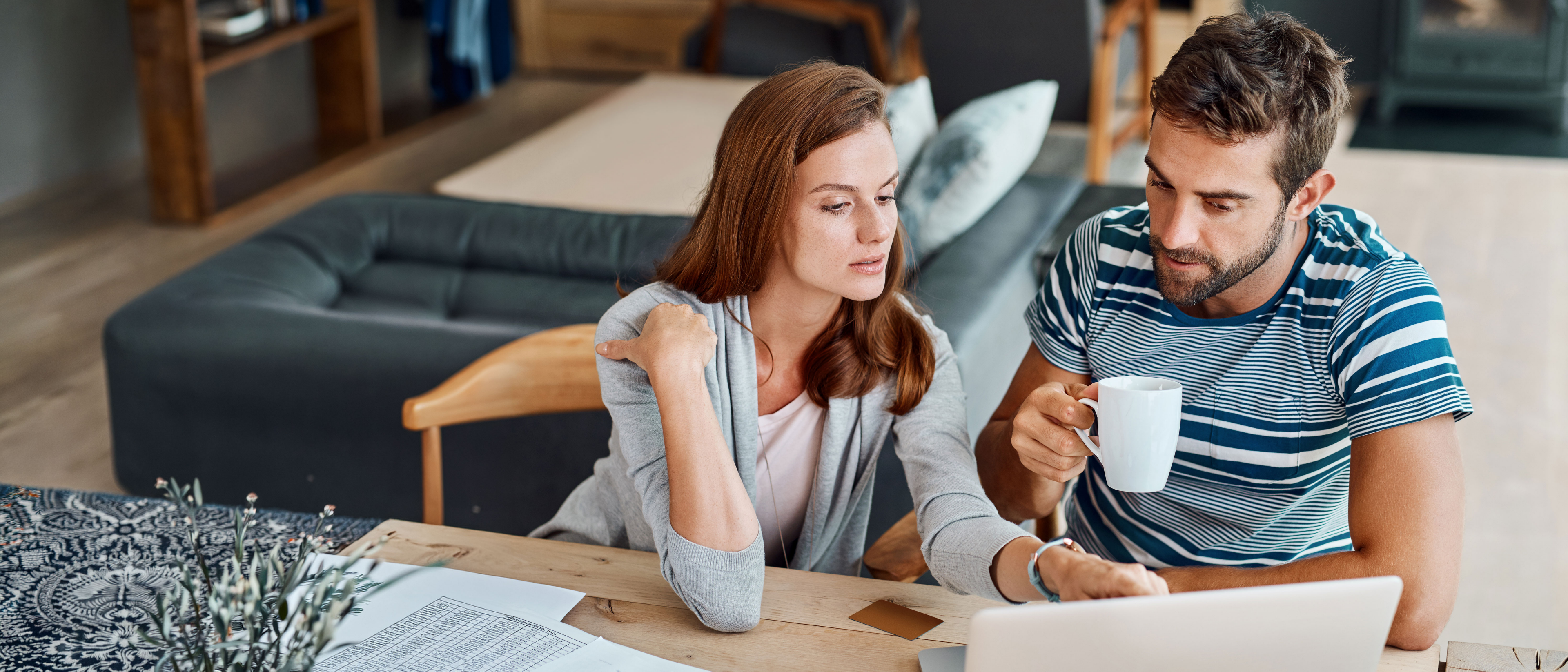 Couple sitting at kitchen counter top looking at bills on computer